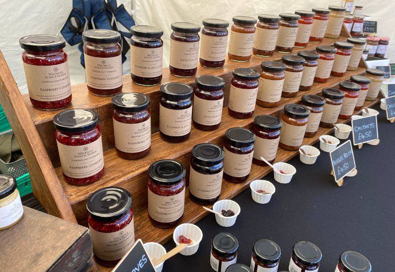 Events An assortment of jars and taster pots from Nichols Pickles & Preserves on table shelfs at a market.